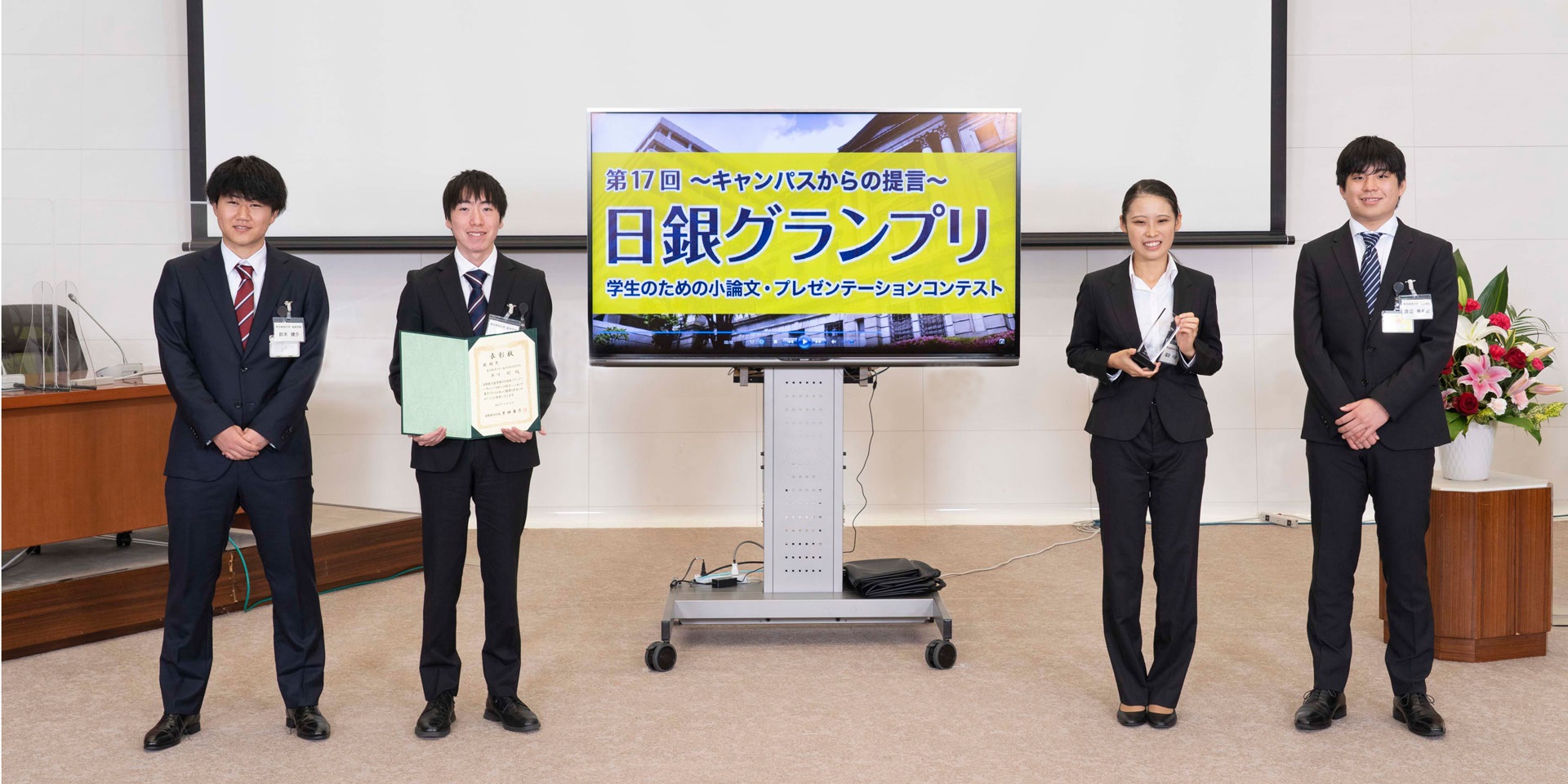 東京経済大学チームの学生4人が、間隔を空けて横一列に起立して記念撮影している様子