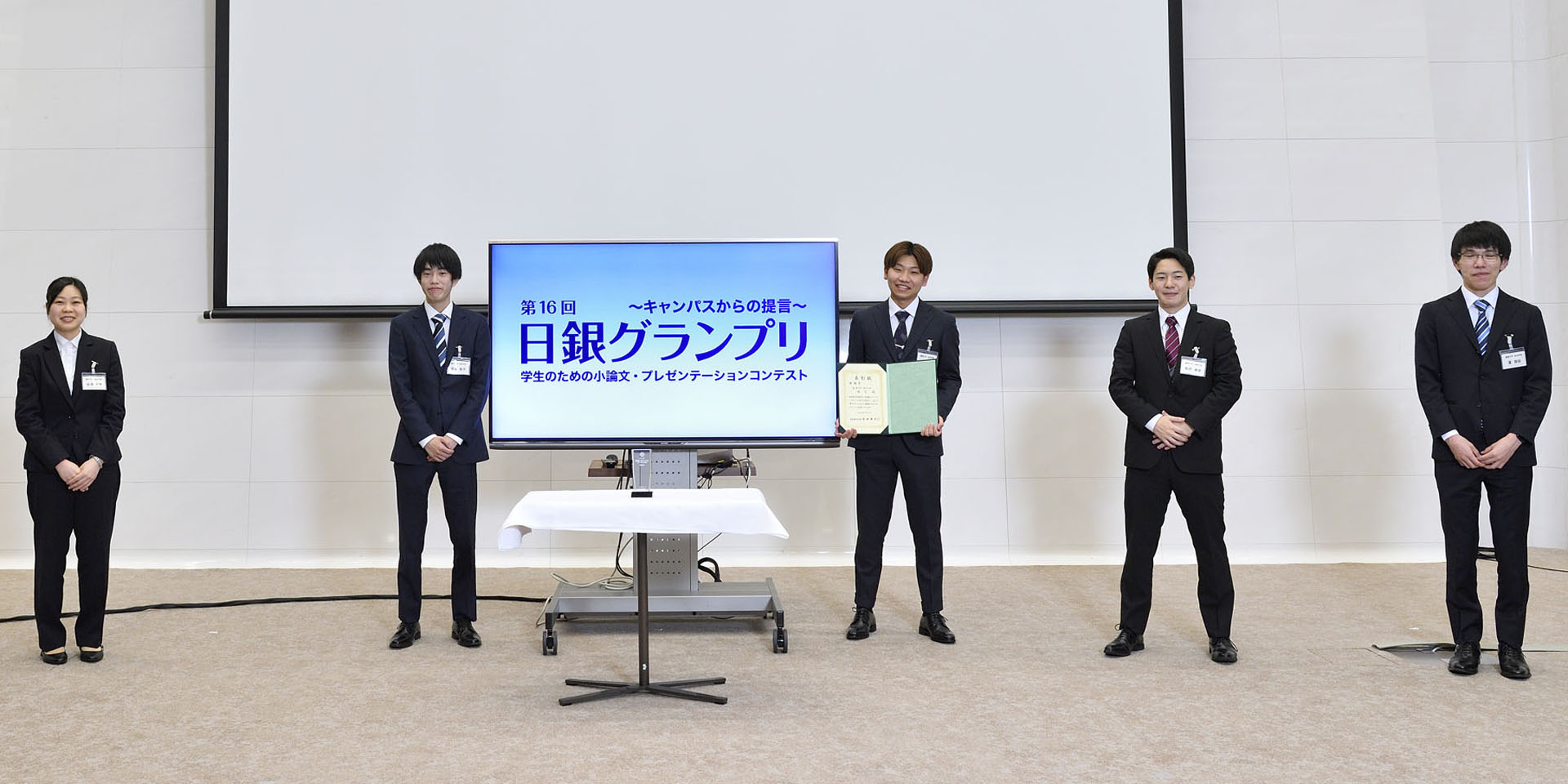麗澤大学チームの学生5名が、間隔を空けて起立して記念撮影をしている様子