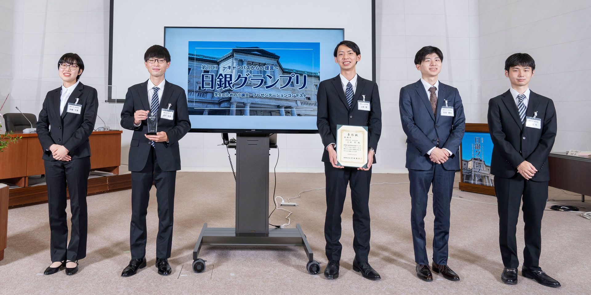 麗澤大学チームの学生5人が、横一列に起立して記念撮影している様子