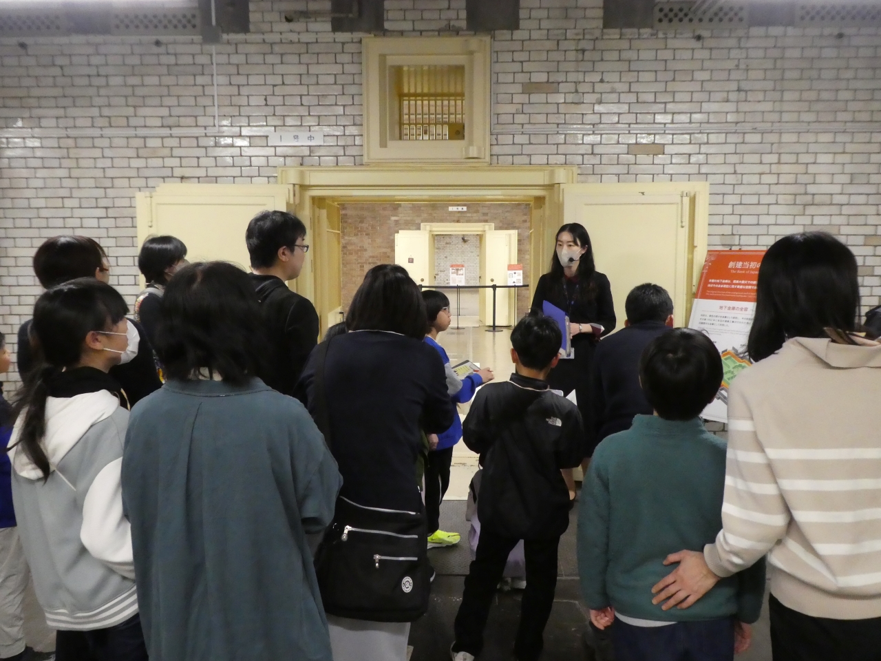 ガイド1人が、参加者20人に対して地下金庫の扉を解説している様子