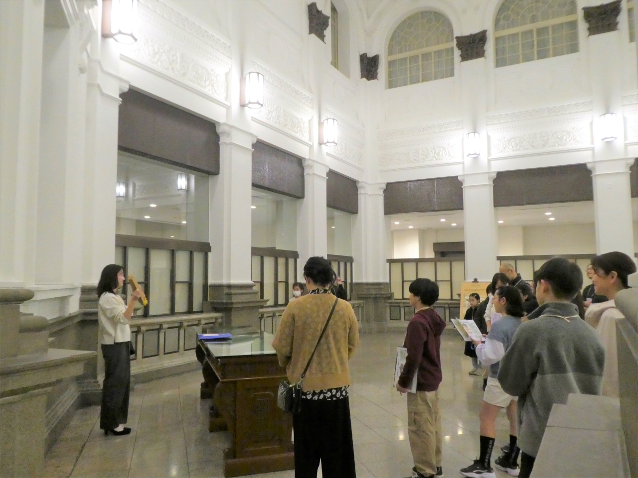 ガイド1人が、参加者20人に客溜にて、建物の説明をしている様子