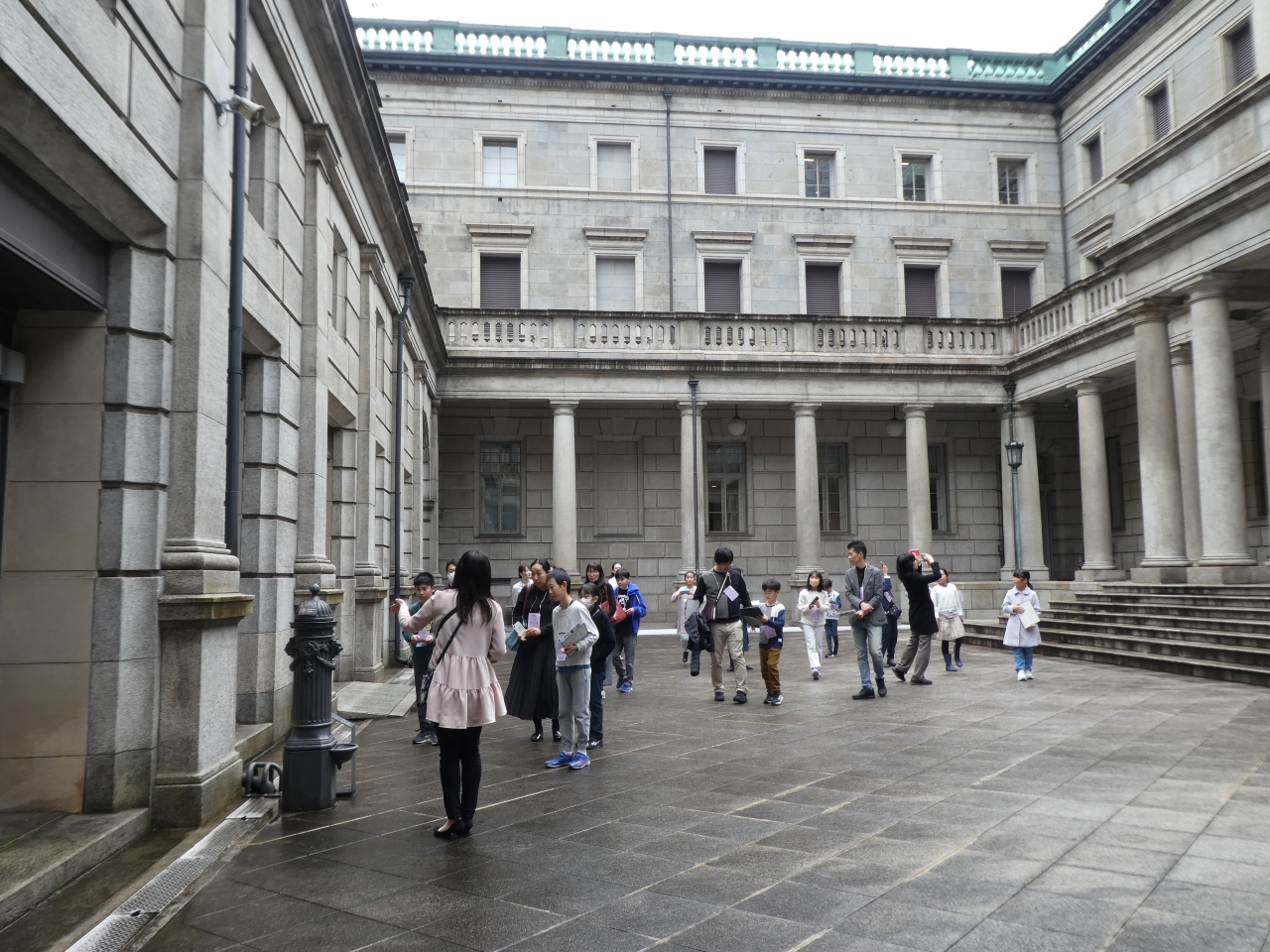 ガイド1人が、参加者20人に中庭にて、馬の水飲み場の説明をしている様子