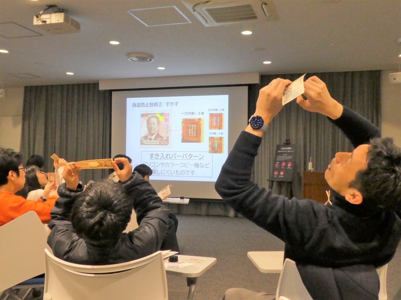 親子(父と息子)2人が、お札を透かしてすき入れバーパターンを確認している様子