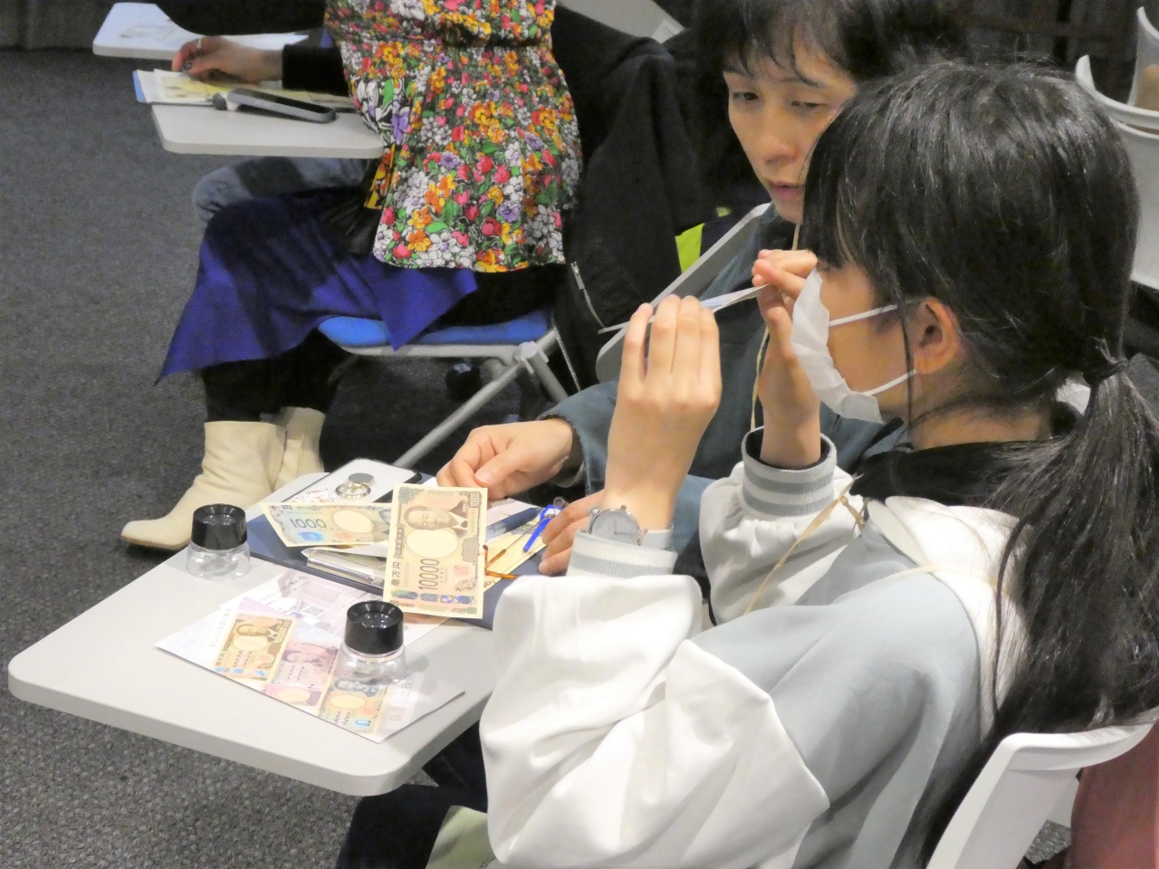 親子(母と娘)2人が、お札を傾けて潜像模様を確認している様子