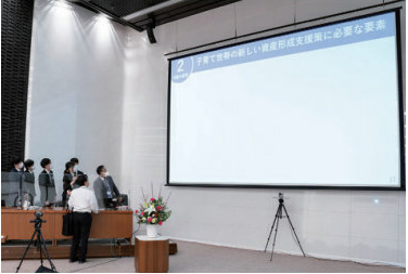 スクリーンに投影されたプレゼン資料を見ながらリハーサルに臨む学生の写真。