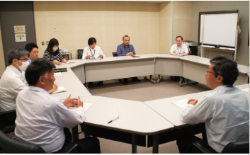 会議室でユニットのメンバー8人が協議している写真。
