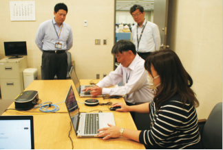 職員4人が、オンラインセミナー等で使用する端末の稼働確認を行っている写真。