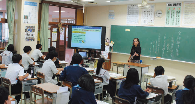 出張授業で講師が教壇に立ち、生徒に説明している様子。