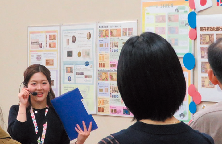 企画展での模様を撮影した写真。展示物の前で職員が参加者に説明を行っている。