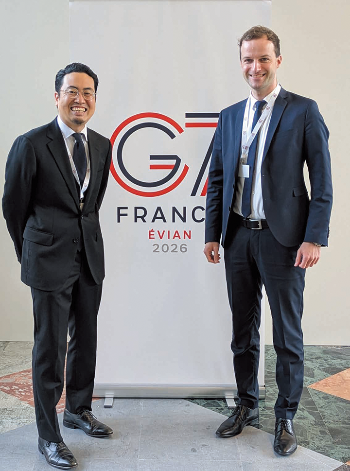 欧州中銀職員と日本銀行職員の写真。G7のロゴの前で笑顔を見せている。
