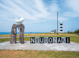 遠くに入道埼灯台を捉えた写真。手前には「NYUDOZAKI」と書かれた碑が見える