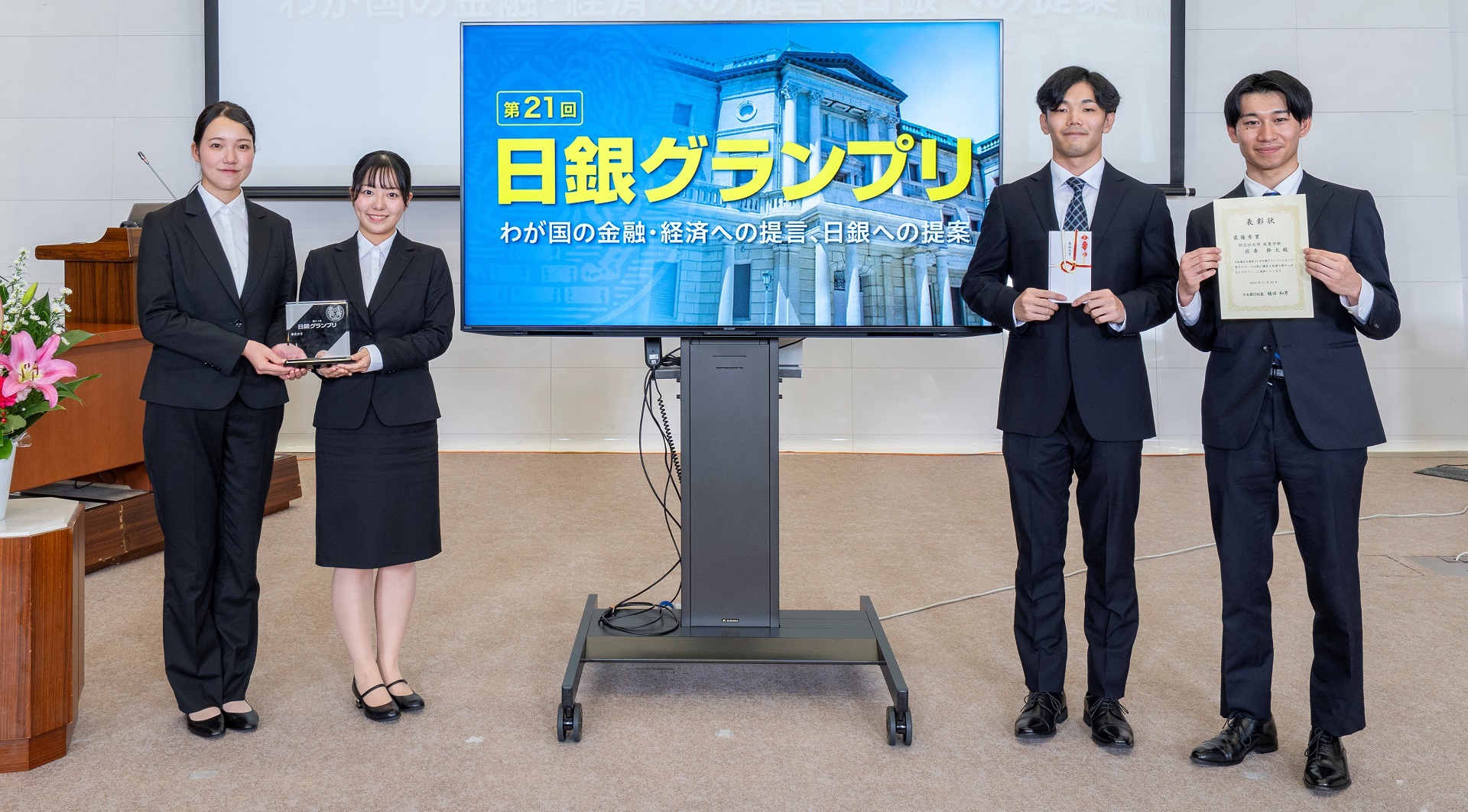 同志社大学政策学部チームの学生4人が、横一列に起立して記念撮影している様子