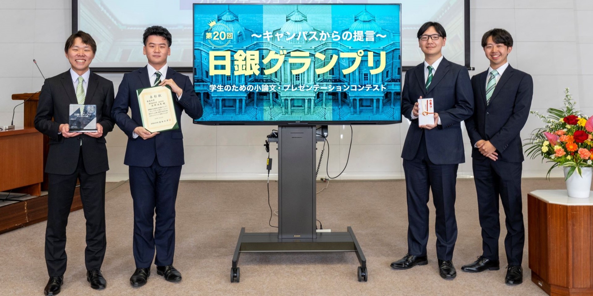 東京経済大学チームの学生4人が、横一列に起立して記念撮影している様子