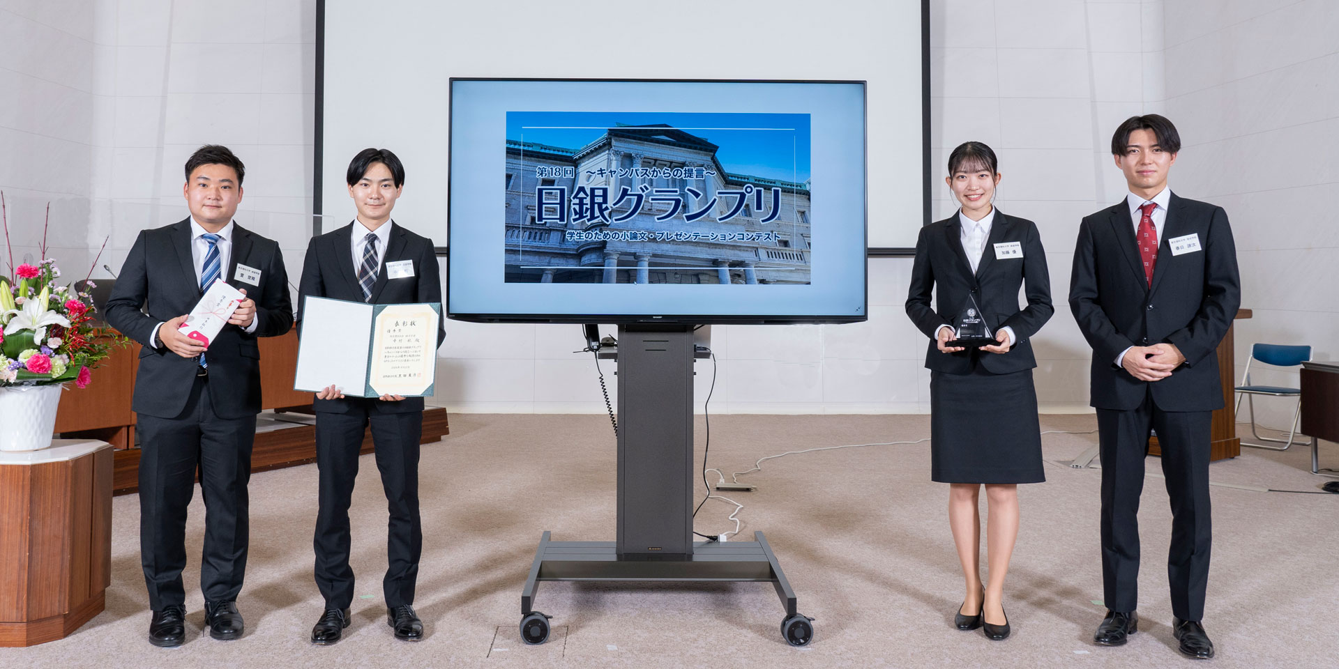 東京理科大学チームの学生4人が、横一列に起立して記念撮影している様子