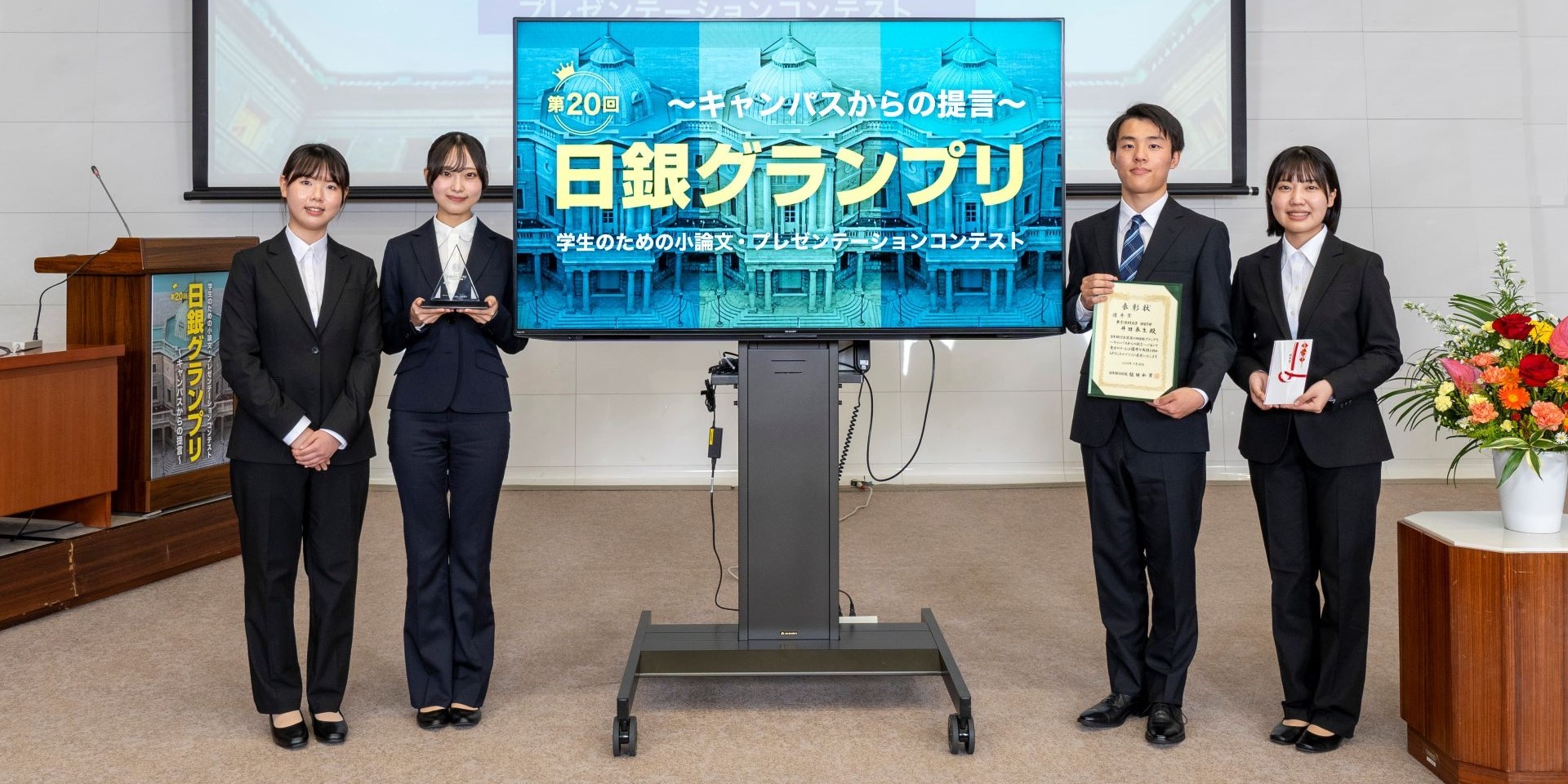 東京理科大学チームの学生4人が、横一列に起立して記念撮影している様子