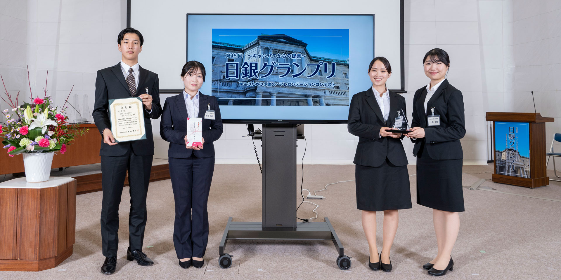 同志社大学チームの学生4人が、横一列に起立して記念撮影している様子