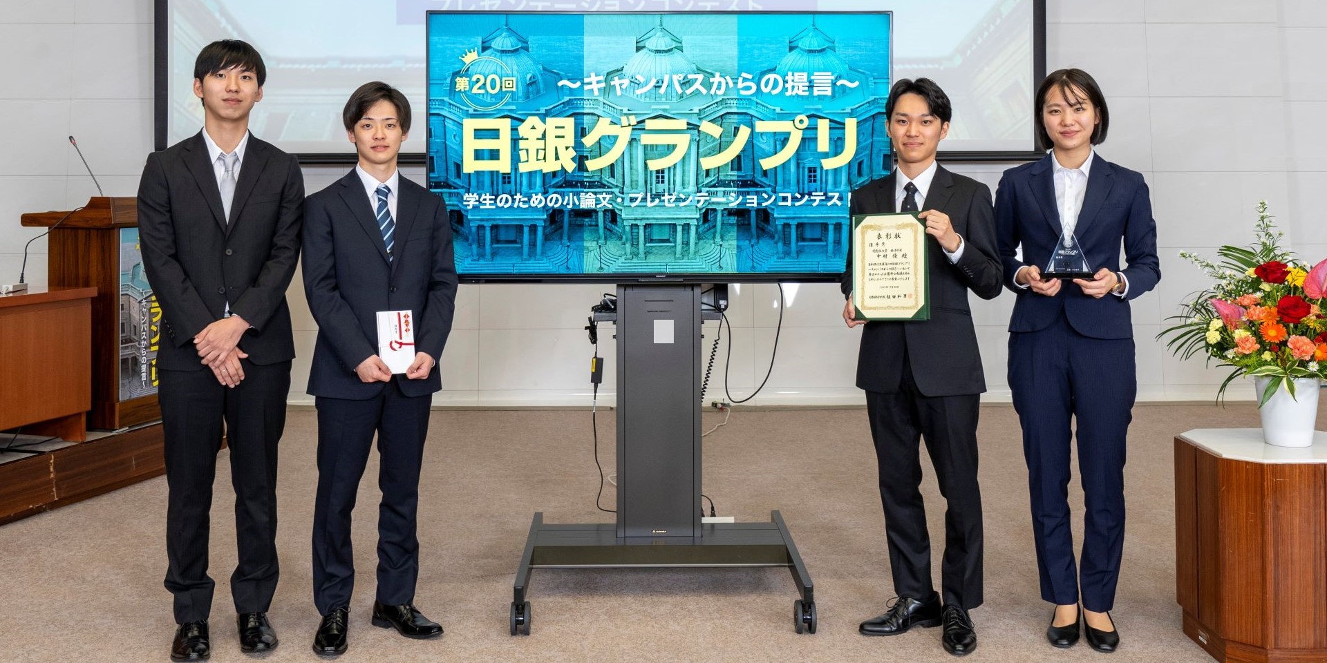 同志社大学チームの学生4人が、横一列に起立して記念撮影している様子