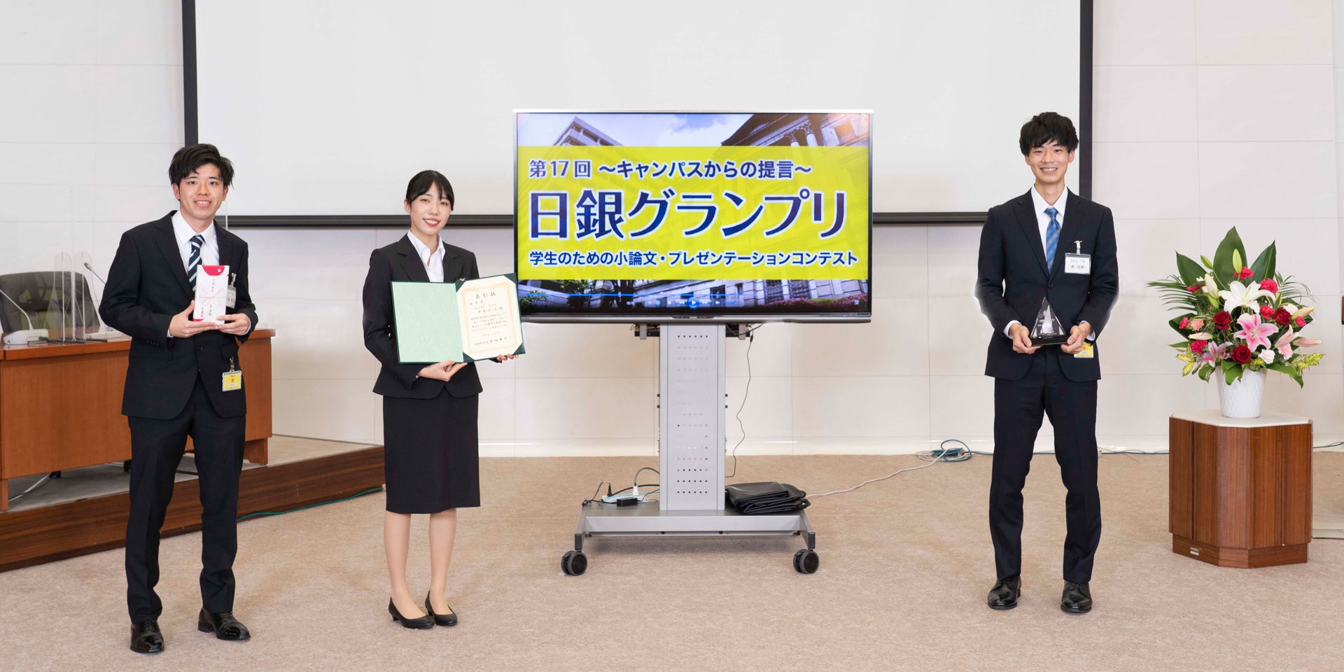明治大学チームの学生3人が、間隔を空けて横一列に起立して記念撮影している様子