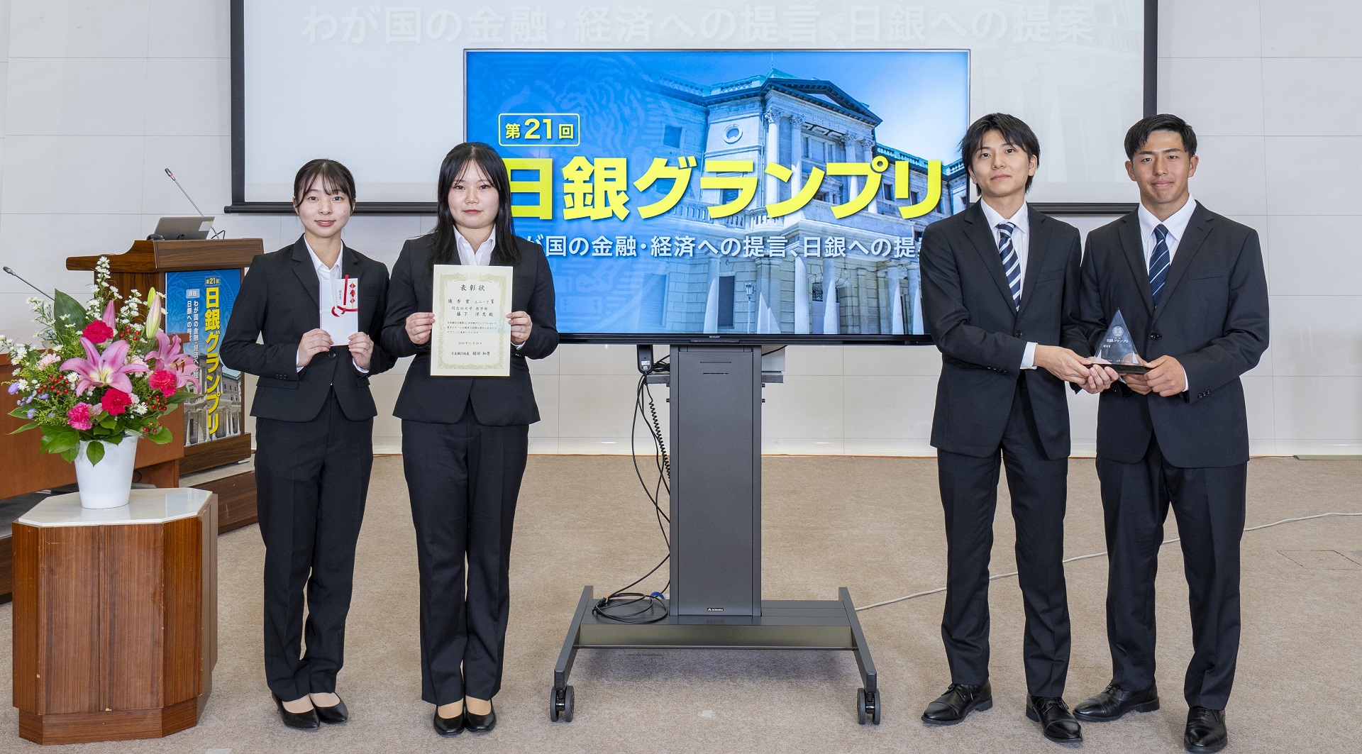 同志社大学商学部チームの学生4人が、横一列に起立して記念撮影している様子