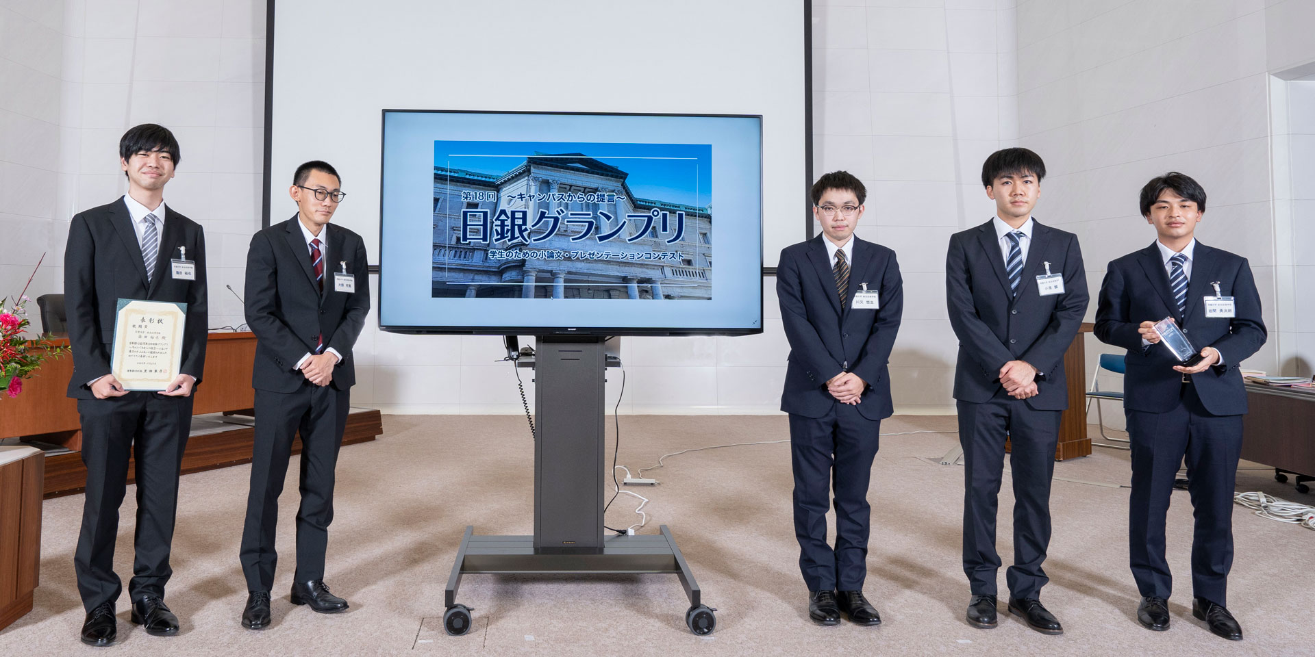常磐大学チームの学生5人が、横一列に起立して記念撮影している様子