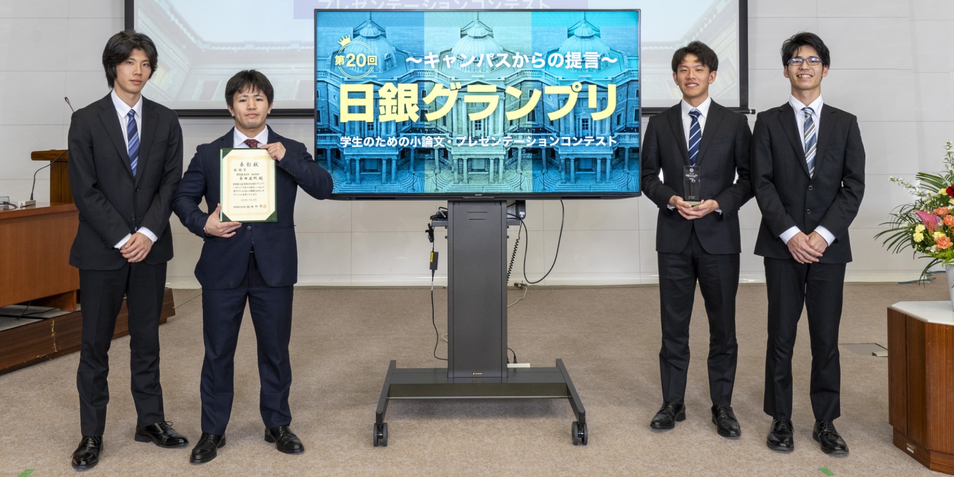 東京経済大学チームの学生4人が、横一列に起立して記念撮影している様子