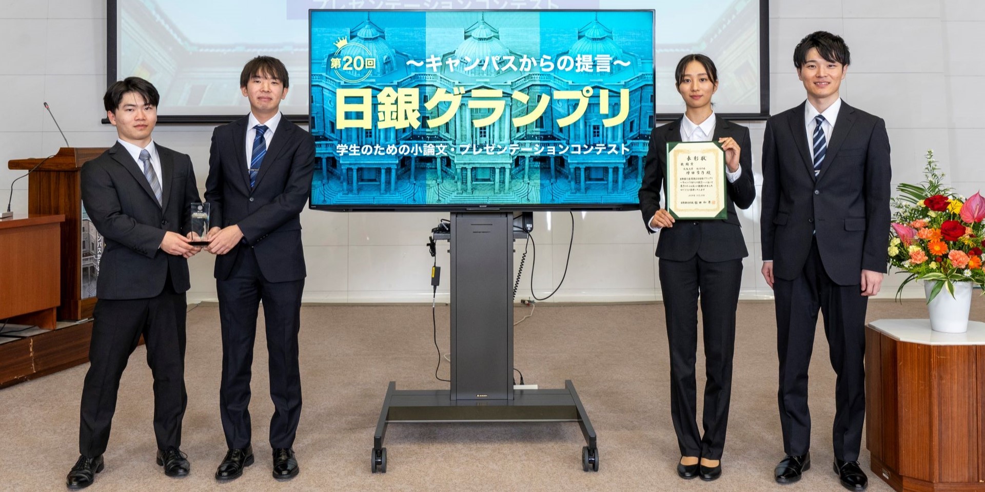 大阪大学チームの学生4人が、横一列に起立して記念撮影している様子