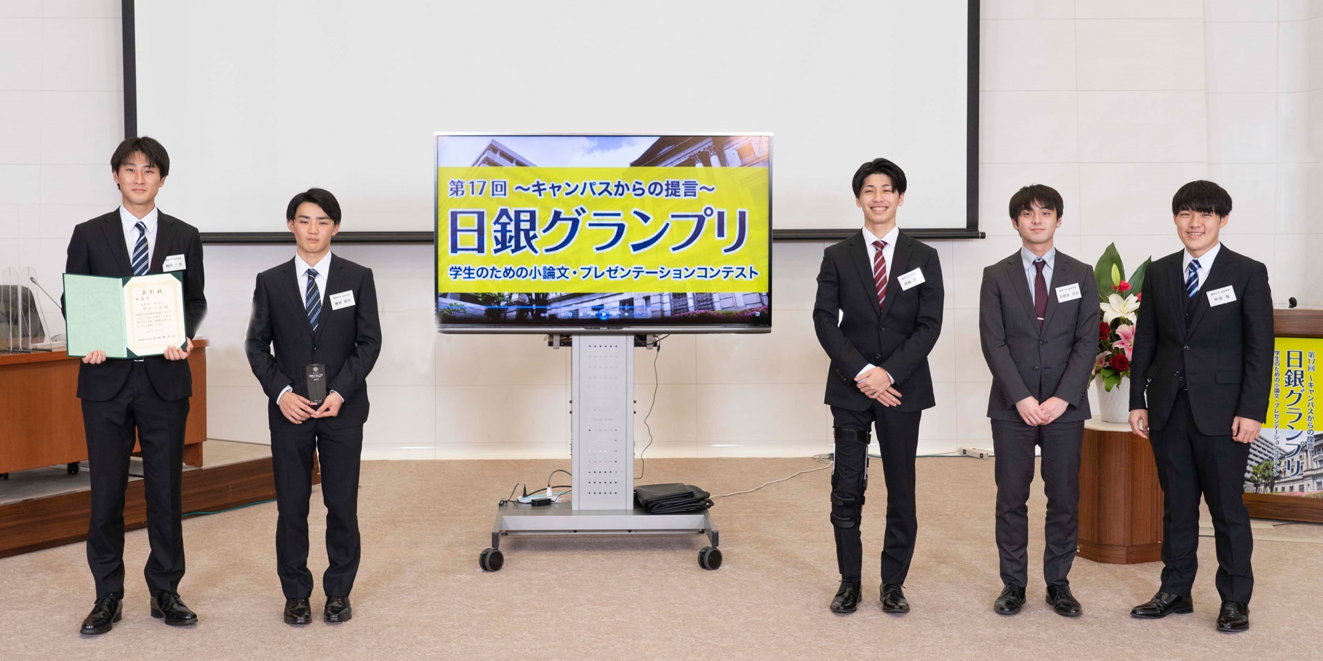 麗澤大学チームの学生5人が、間隔を空けて横一列に起立して記念撮影している様子