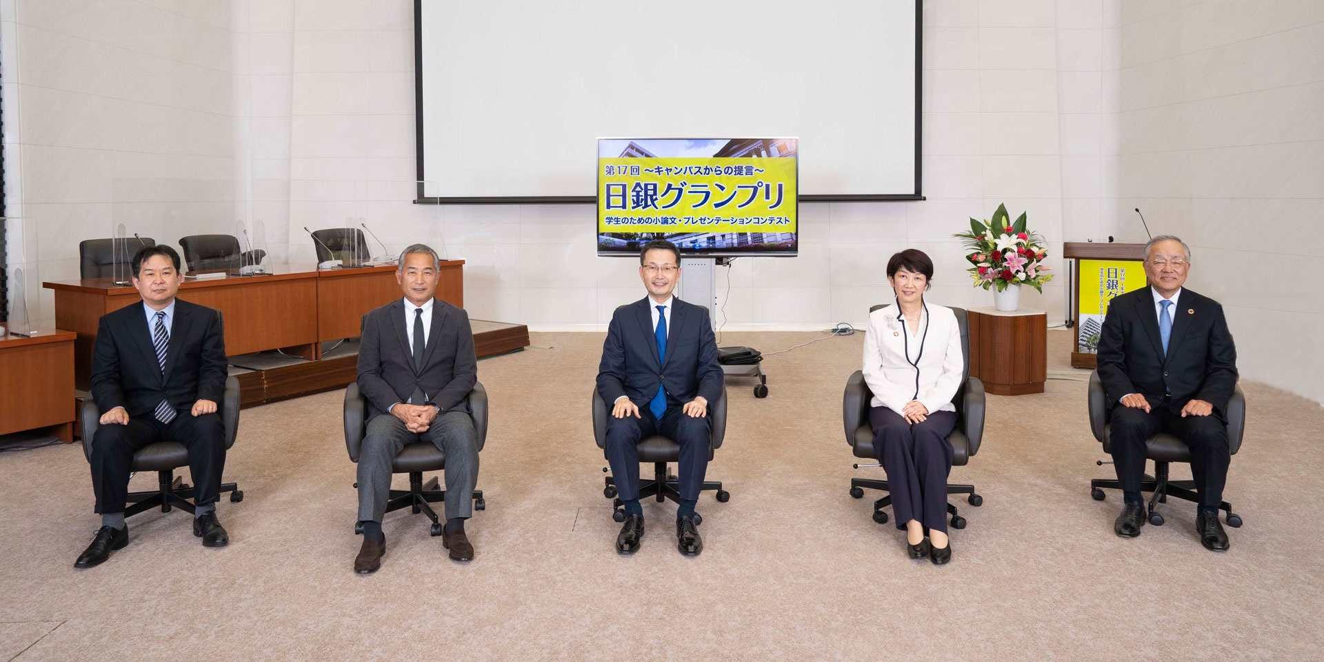5人の審査員が、間隔を空けて横一列に着席して記念撮影している様子