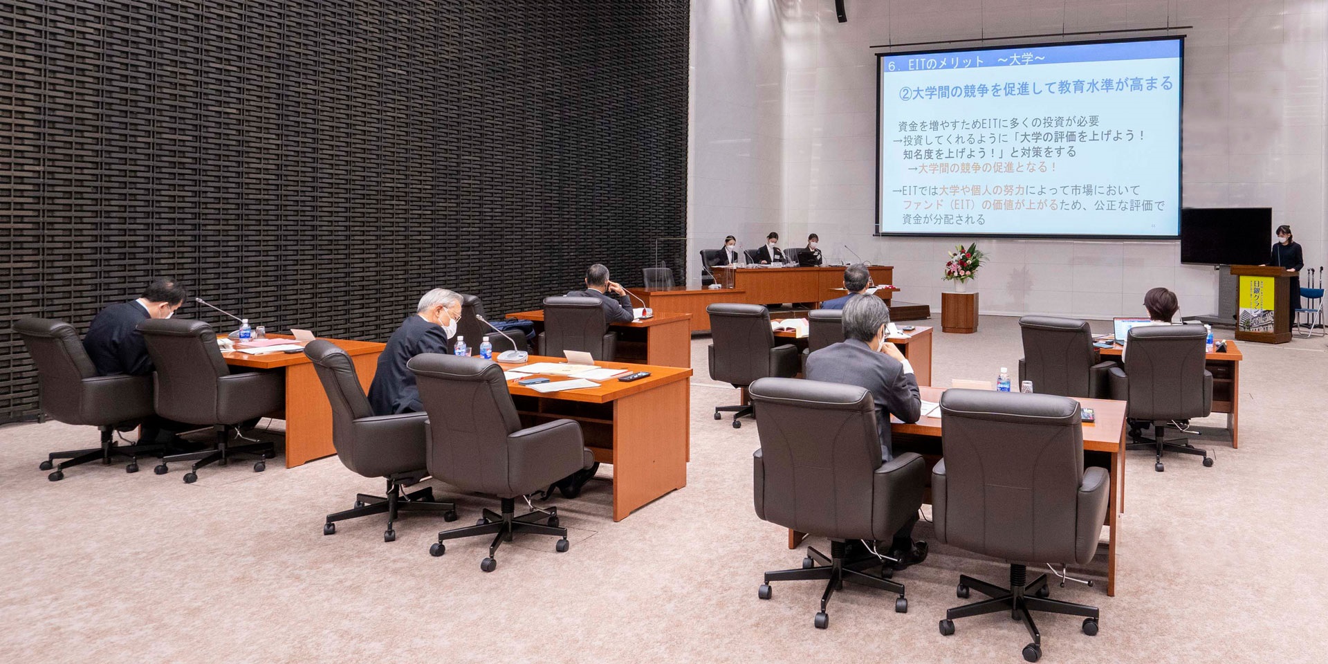 審査員5人が、審査会場内の大きなスクリーンに投影された資料を見ながら、学生チームによるプレゼンテーションを聞いている様子