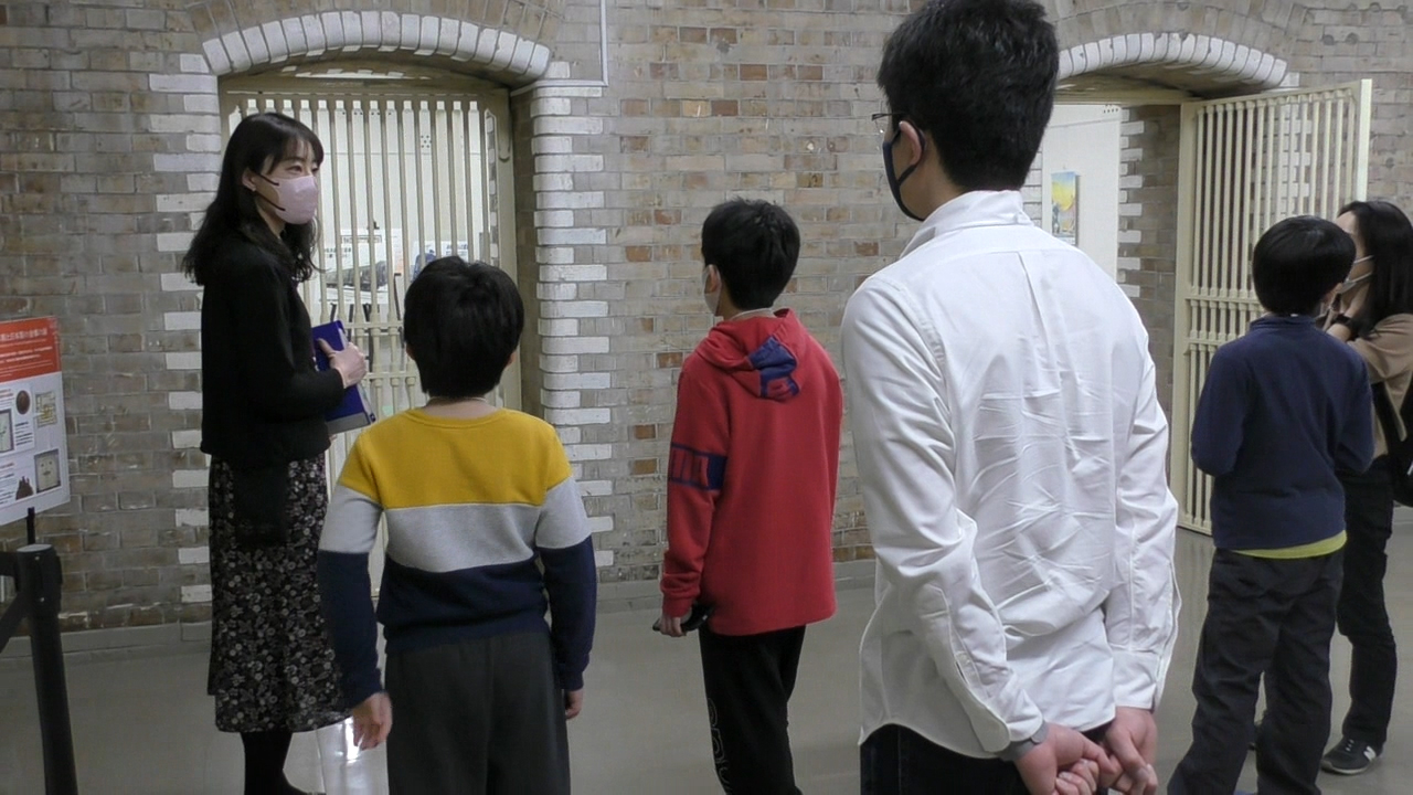 地下金庫内にいる参加者5人が、案内者1人による解説を聞いている様子