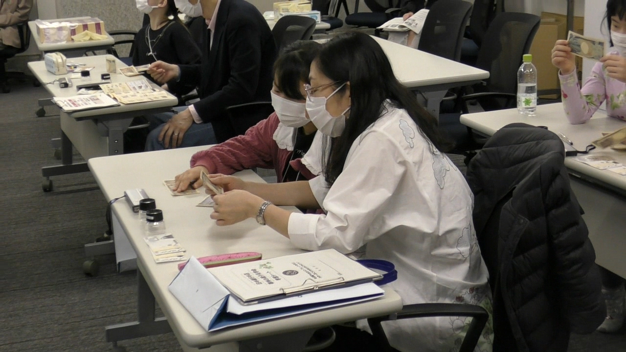 会場内にいる参加者2人が、お札を傾けながら潜像模様を確認している様子