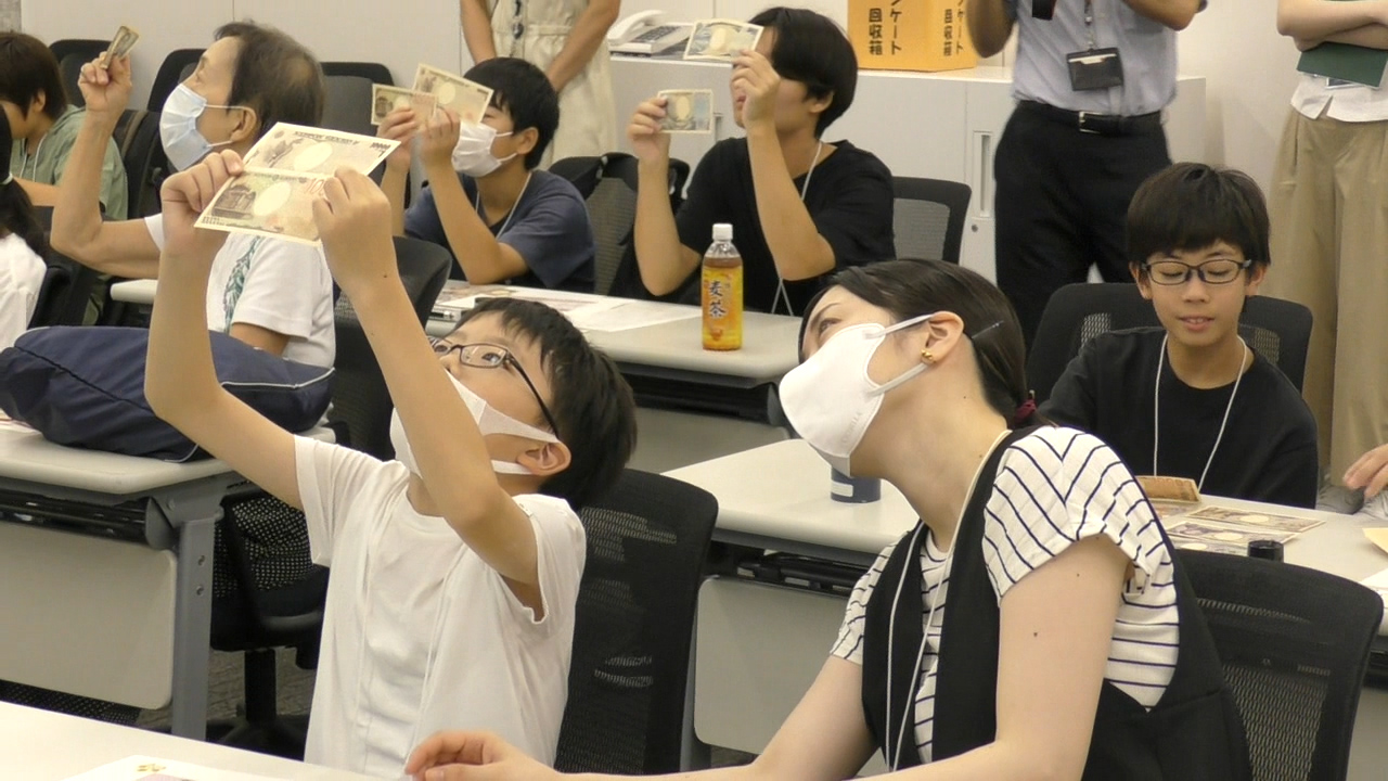 参加者6人が、お札を掲げ、お札のすかしを確認している様子