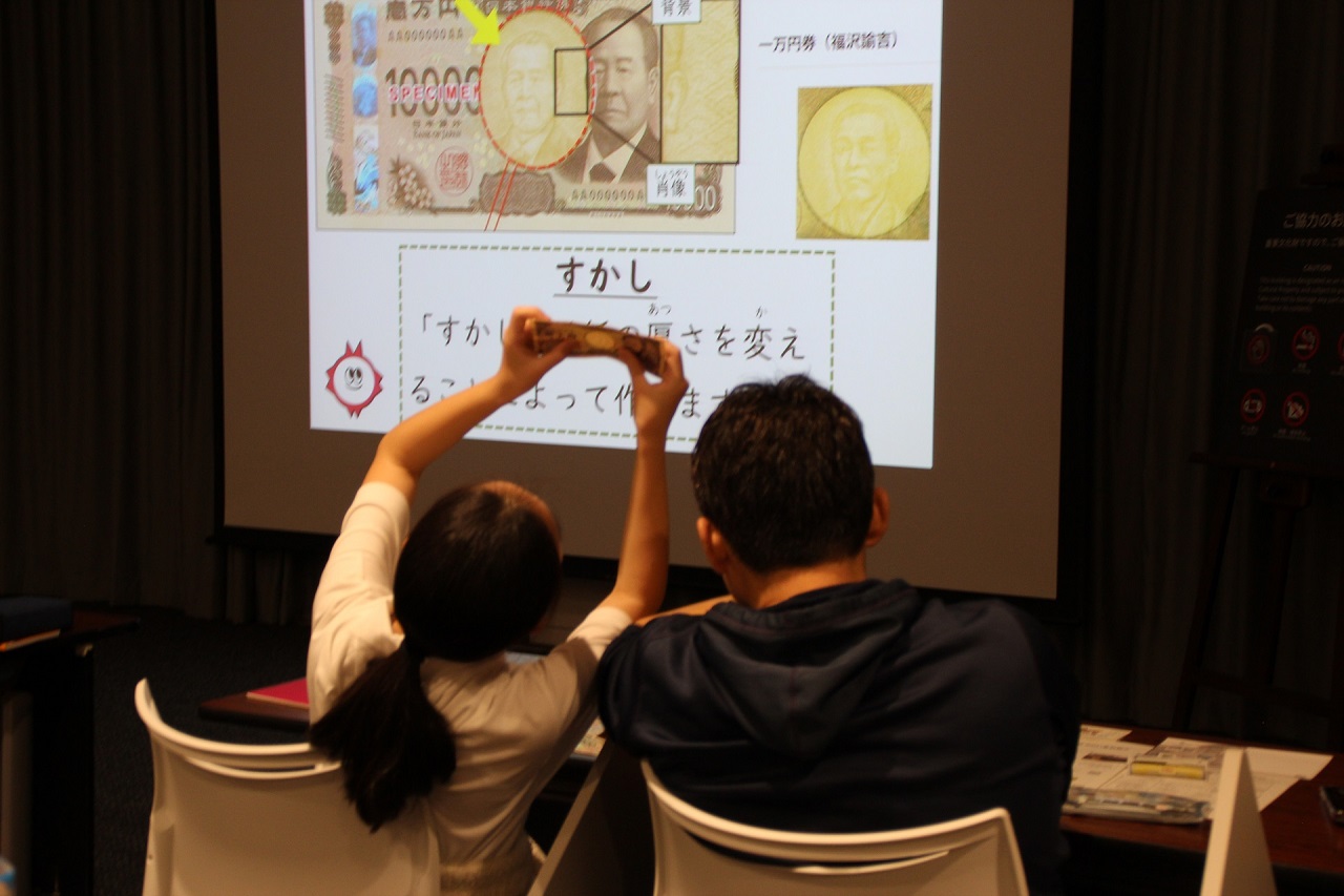 親子（父と娘）2人が、お札を掲げ、すかしを確認している様子