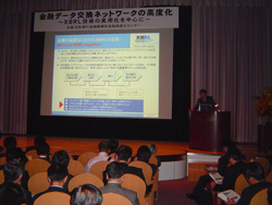セミナー参加者とステージ上のパネリストとスクリーンを会場の後方から撮影した写真