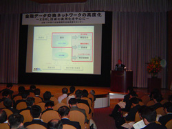 セミナー参加者とステージ上のパネリストとスクリーンを会場の後方遠方から撮影した写真