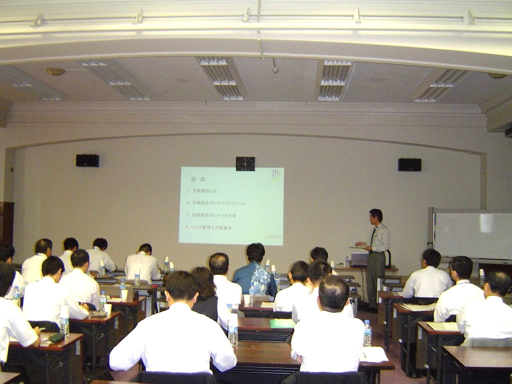 スライドを使って講演しているパネリストとセミナー参加者を会場の後方から撮影した写真
