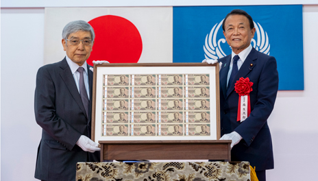 20枚1面で印刷され、額に入った新一万円券を麻生財務大臣と黒田総裁が手に取って記念撮影している写真